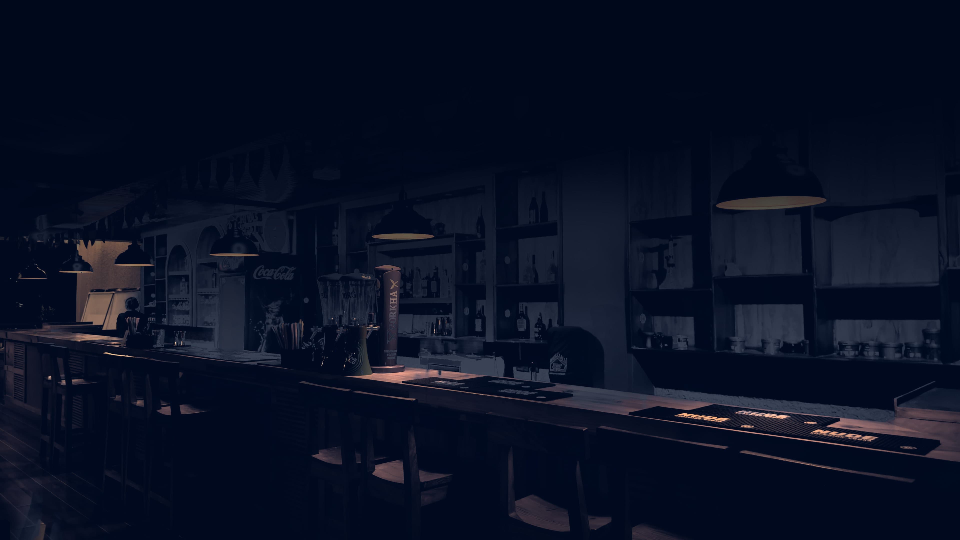 The Lekavya Lounge bar after dark — a long timber counter and stools receding into the room, pendant lamps throwing warm pools over the back shelving, bunting strung along the ceiling
